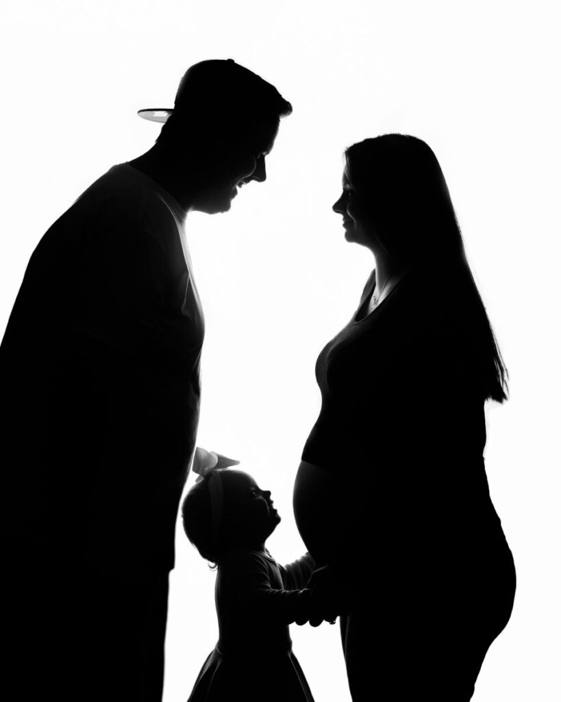 Silhouette maternity portrait with parents and young child touching baby bump