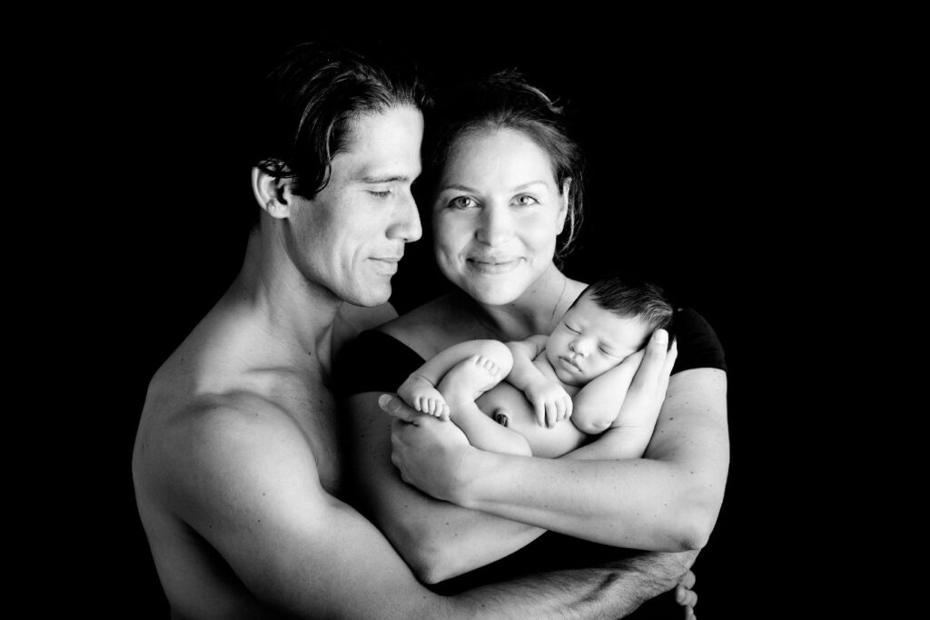 Parents holding sleeping newborn during black and white studio portrait.
