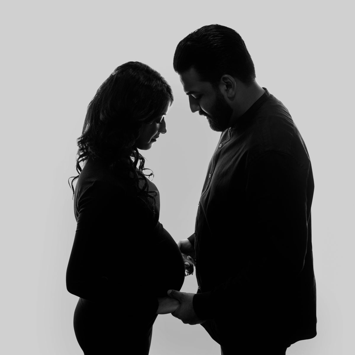 Black and white maternity couple portrait with expecting parents holding baby bump in studio silhouette pose