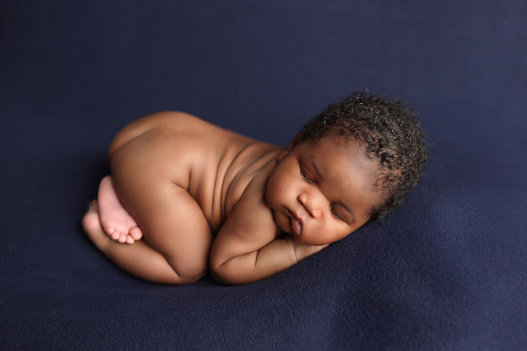 Sleeping newborn baby curled up on a dark blue blanket during a studio portrait session