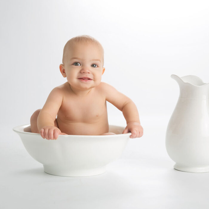 Six month old baby sitting in white porcelain bowl during milestone session