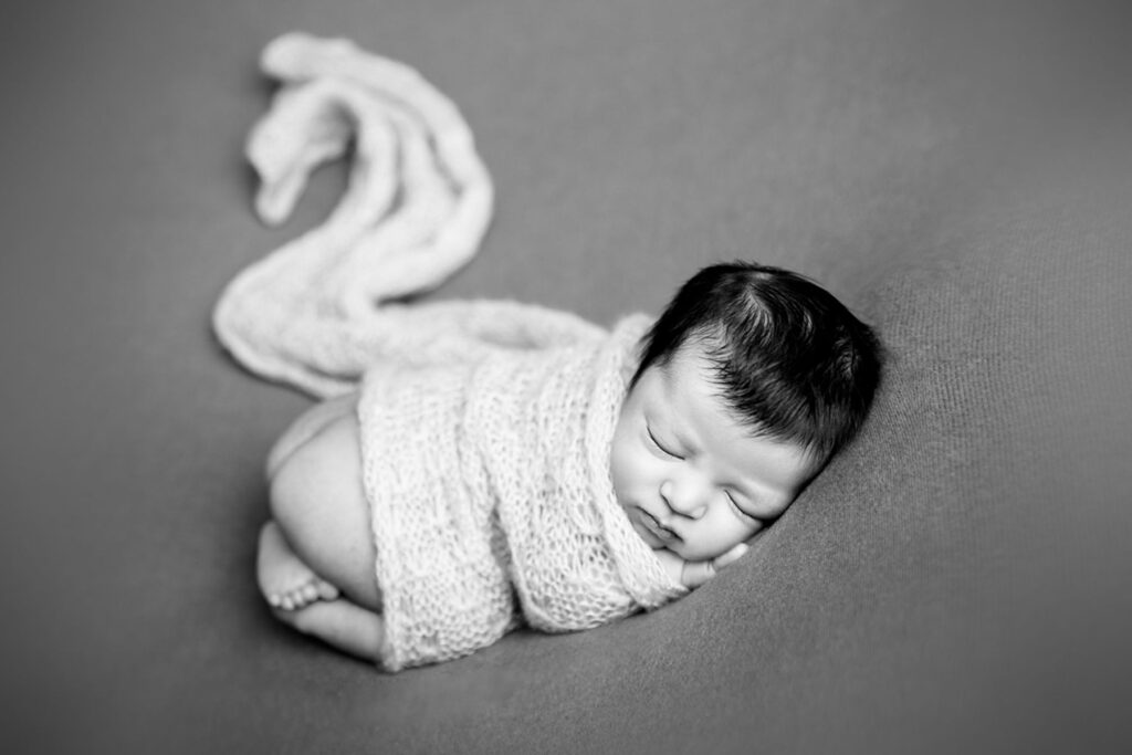 Sleeping newborn baby wrapped in a swan-inspired shape created by wrap in a black and white portrait
