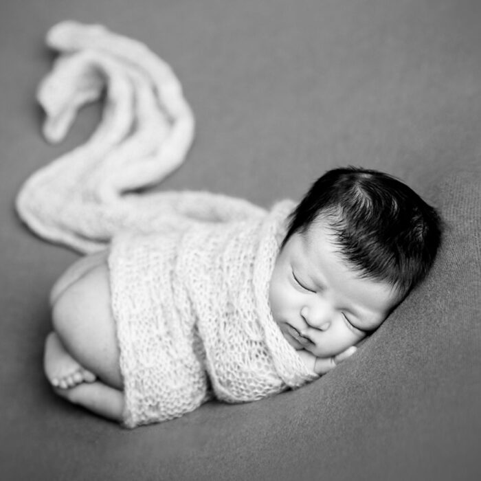Sleeping newborn baby wrapped in a swan-inspired shape created by wrap in a black and white portrait