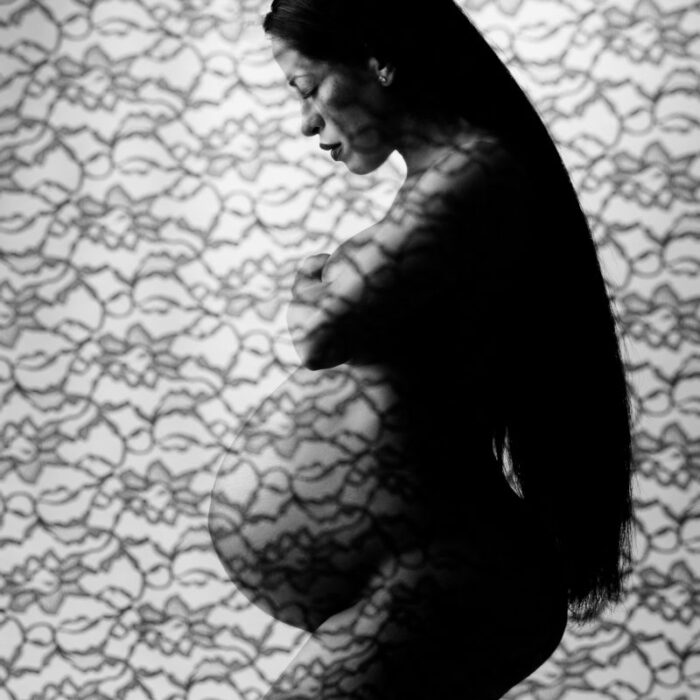 Artistic black and white maternity silhouette portrait featuring patterned lace and an expectant mother