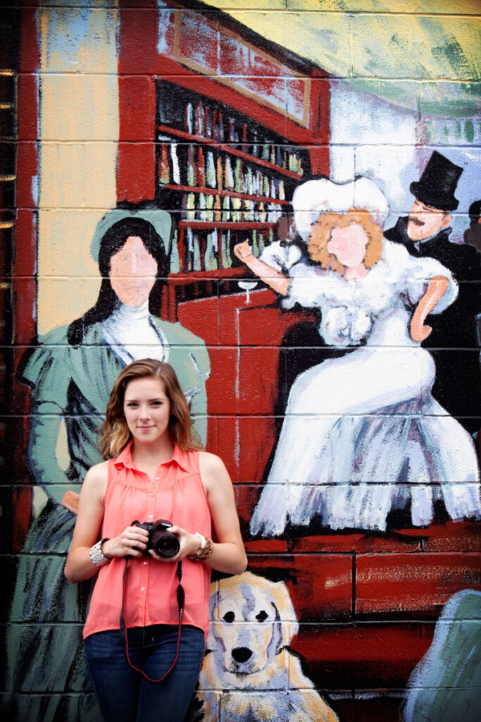 High school senior holding camera in front of colorful mural.