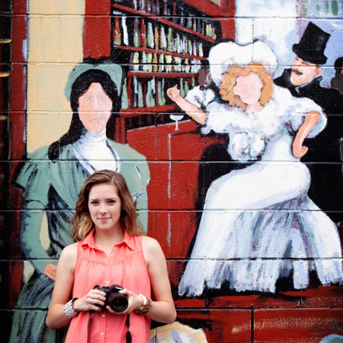High school senior holding camera in front of colorful mural.