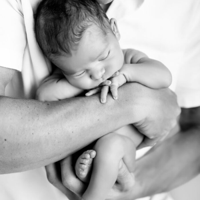 Father holding sleeping newborn baby in black and white portrait