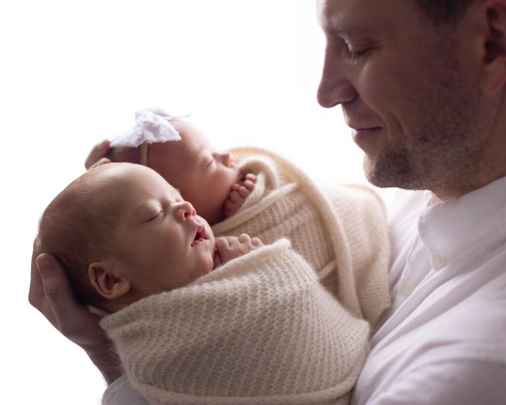 Father holding sleeping newborn twins wrapped in blankets.