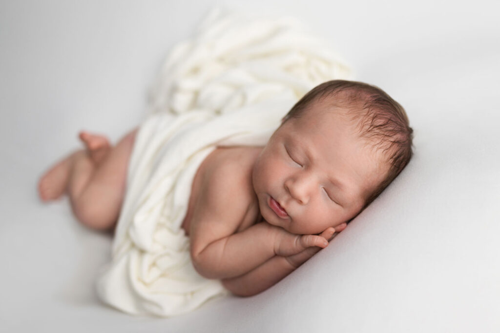 Sleeping newborn wrapped in cream fabric on a soft neutral backdrop