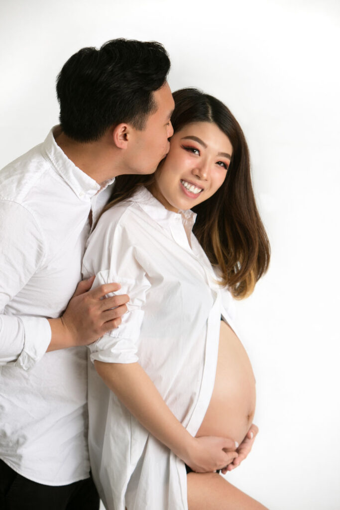 Expectant couple embracing during a studio maternity session in coordinated white clothing
