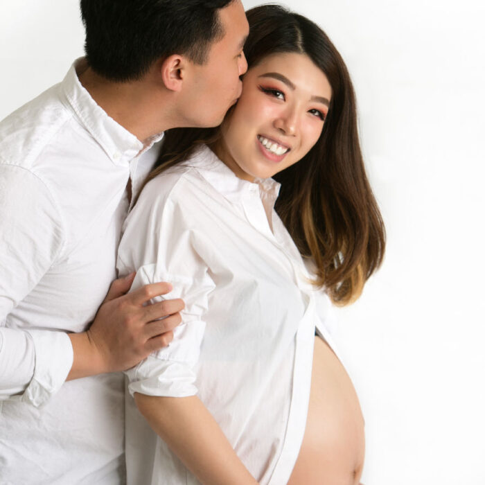 Expectant couple embracing during a studio maternity session in coordinated white clothing