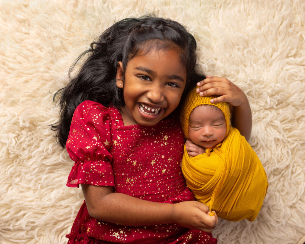 Smiling big sister holding a sleeping newborn baby during a sibling portrait session
