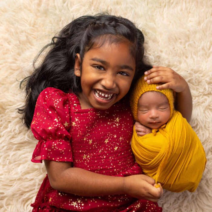 Smiling big sister holding a sleeping newborn baby during a sibling portrait session