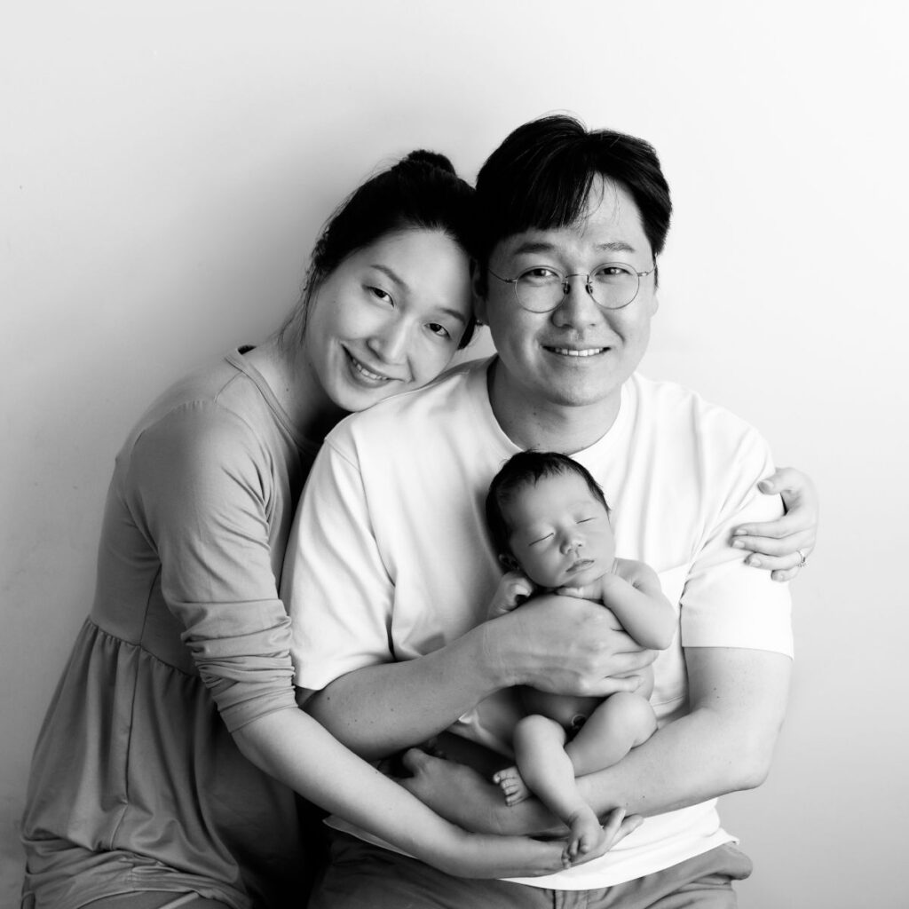 Parents smiling while holding their sleeping newborn baby during a black and white portrait session