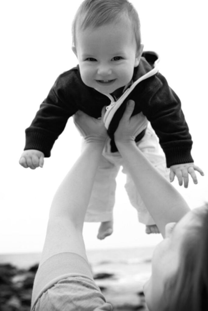 Parent lifting smiling baby into the air during playful black and white portrait session.