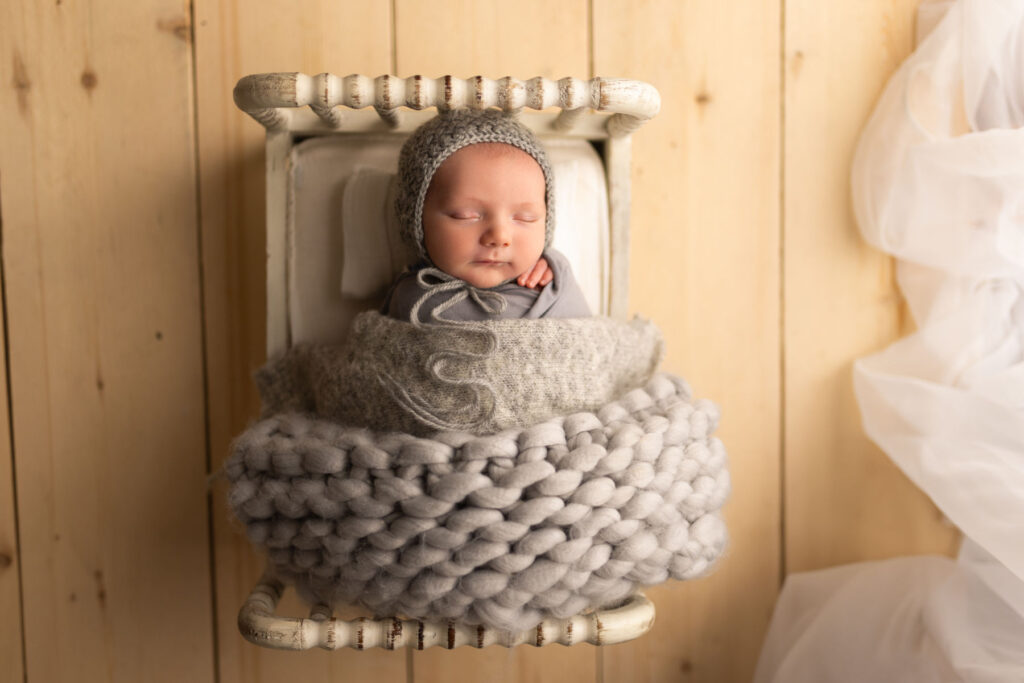 Sleeping newborn baby wrapped in gray fabric on a white wood bed during a studio session