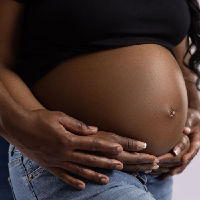 Close-up maternity portrait with parents gently holding a pregnant belly