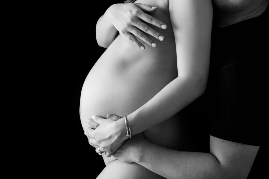 Black and white maternity portrait featuring hands gently cradling a baby bump