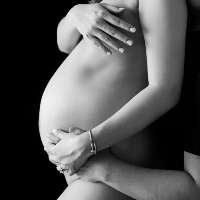 Black and white maternity portrait featuring hands gently cradling a baby bump