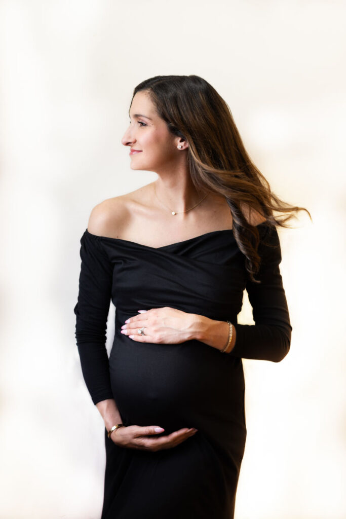 Expecting mother in elegant black dress with long hair blowing during maternity photography session