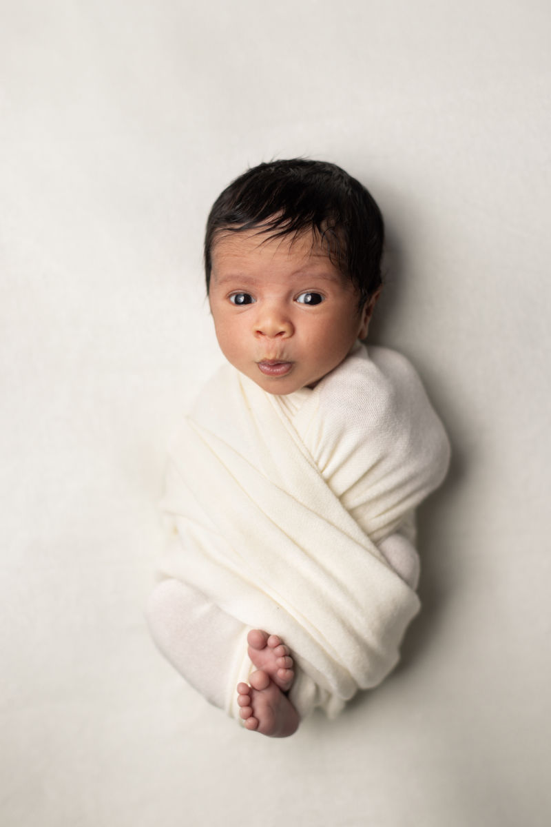 Awake newborn baby wrapped in soft cream fabric against a neutral background