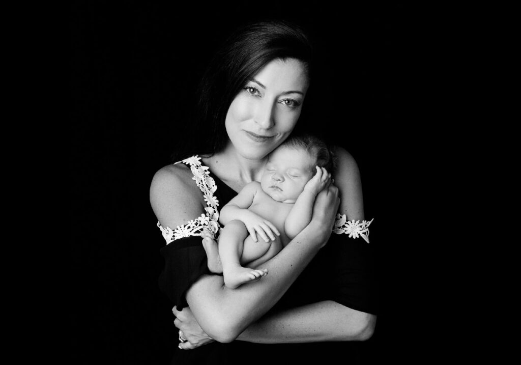 Mother holding sleeping newborn in black and white portrait.