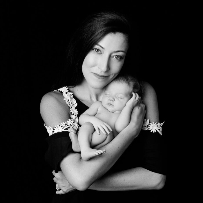 Mother holding sleeping newborn in black and white portrait.