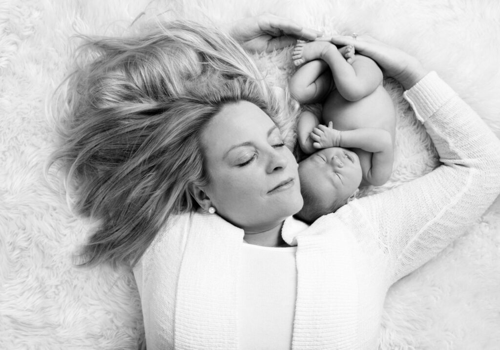 Mother lying beside her newborn baby during a black-and-white newborn photography session