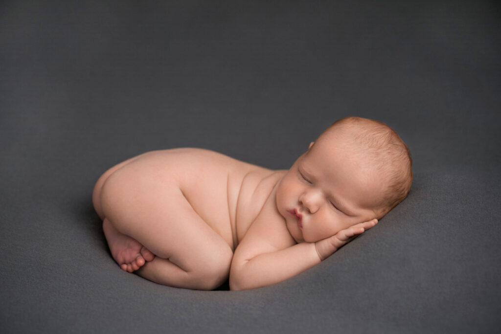 Sleeping newborn baby posed on a soft grey backdrop during a studio session