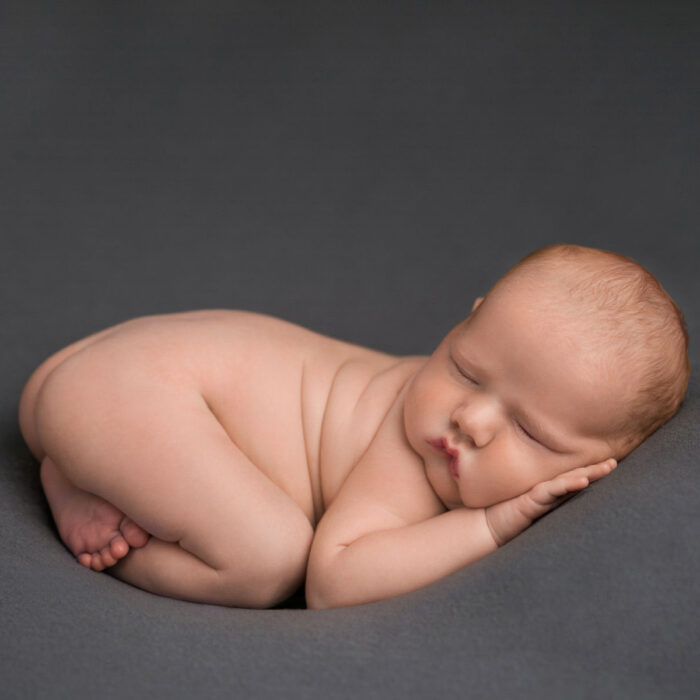 Sleeping newborn baby posed on a soft grey backdrop during a studio session
