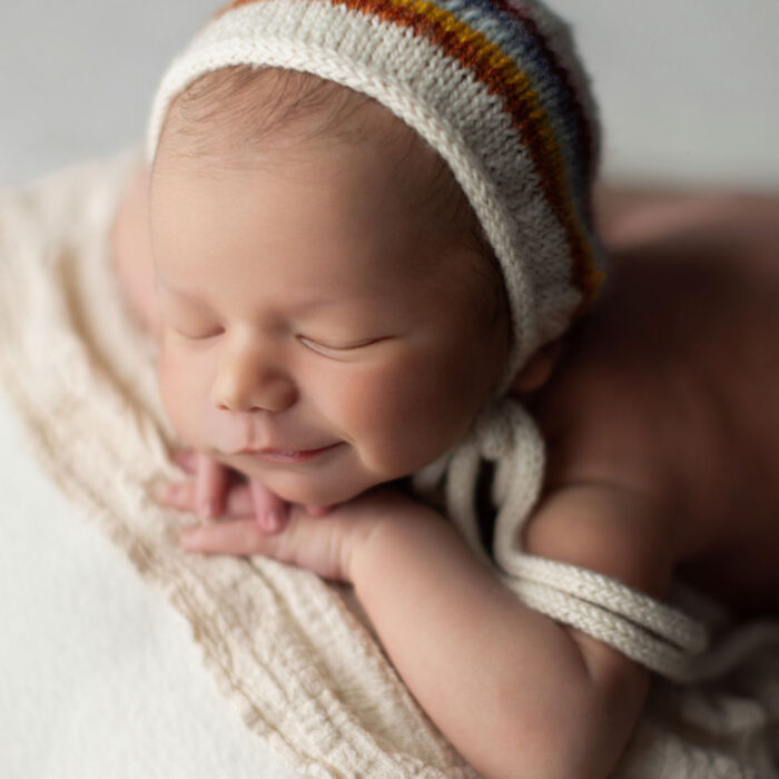 Sleeping newborn baby smiling while wearing a striped knit hat