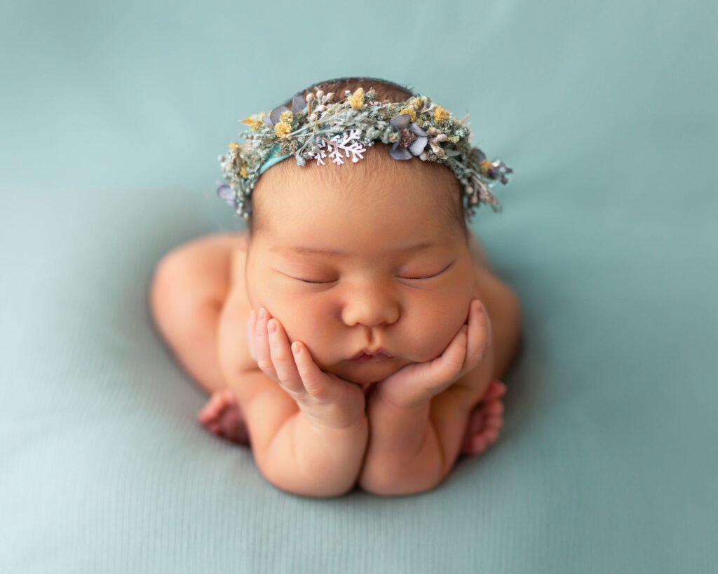 Sleeping newborn baby wearing a floral headband on a soft teal background