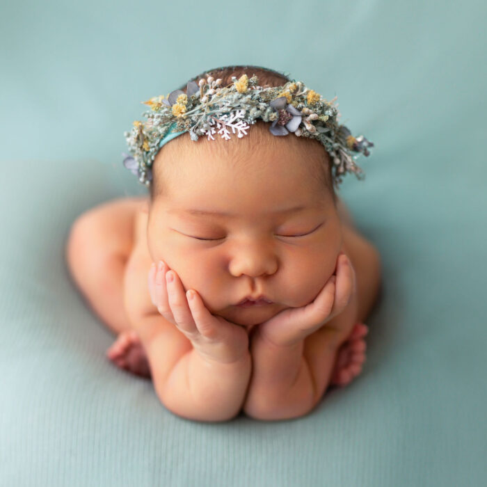 Sleeping newborn baby wearing a floral headband on a soft teal background