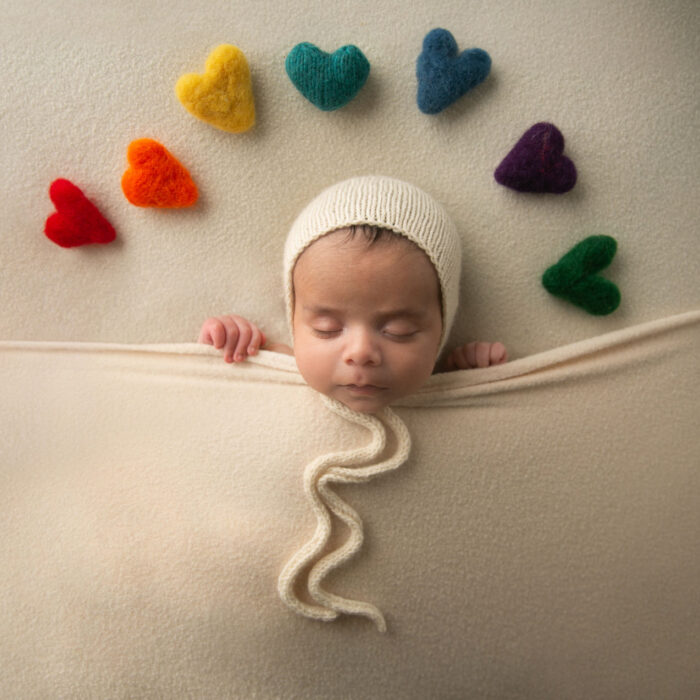 Sleeping newborn baby tucked beneath a blanket surrounded by colorful heart decorations
