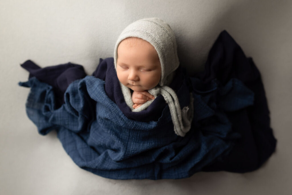 Sleeping newborn baby wrapped in blue fabric with a soft knit bonnet