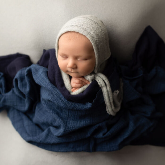 Sleeping newborn baby wrapped in blue fabric with a soft knit bonnet