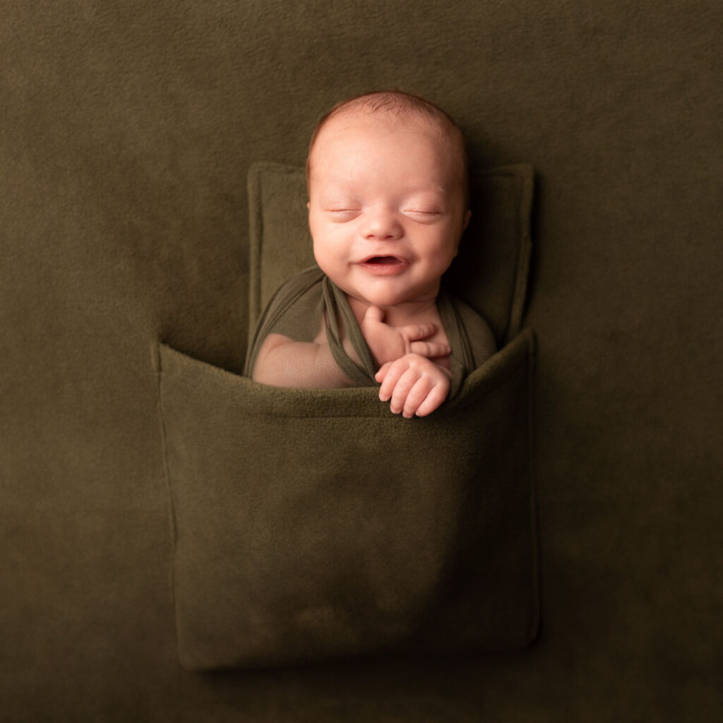 Smiling newborn baby wrapped in green fabric during a studio portrait session