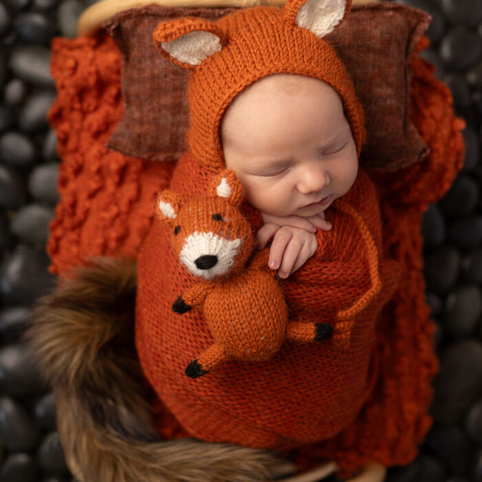Sleeping newborn baby in a fox themed portrait setup with warm fall colors