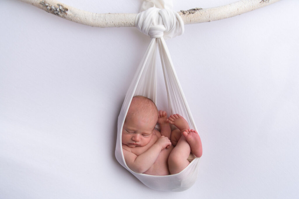 Sleeping newborn baby posed in a white fabric wrap during a studio photography session