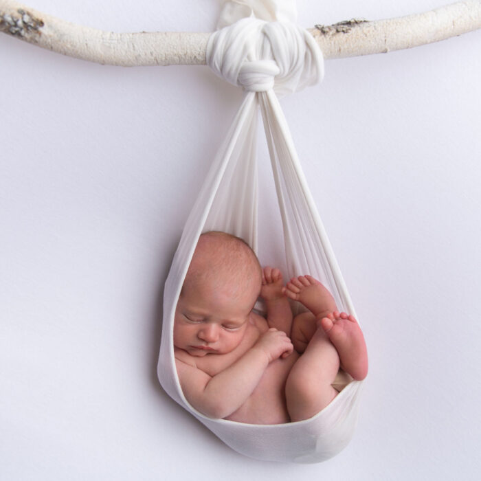 Sleeping newborn baby posed in a white fabric wrap during a studio photography session
