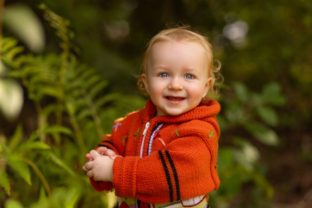 Smiling toddler wearing an orange sweater during an outdoor child portrait session