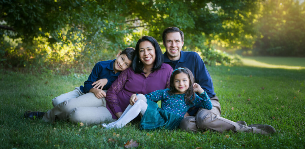 Family of four sitting in grassy field during outdoor family photography session at sunset