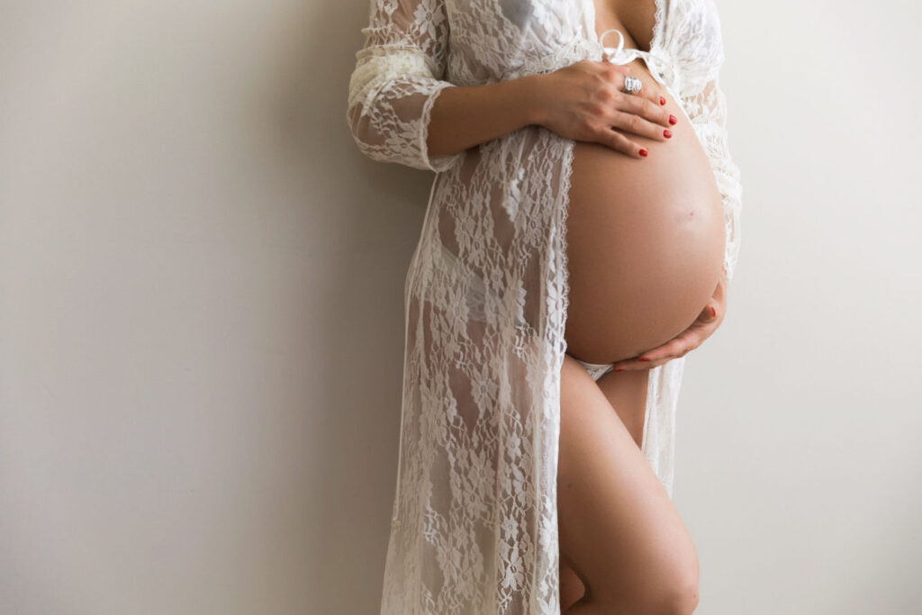Pregnant mother wearing white lace while holding her baby bump during a maternity session