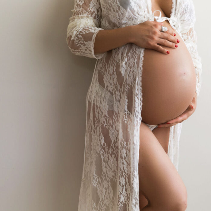 Pregnant mother wearing white lace while holding her baby bump during a maternity session