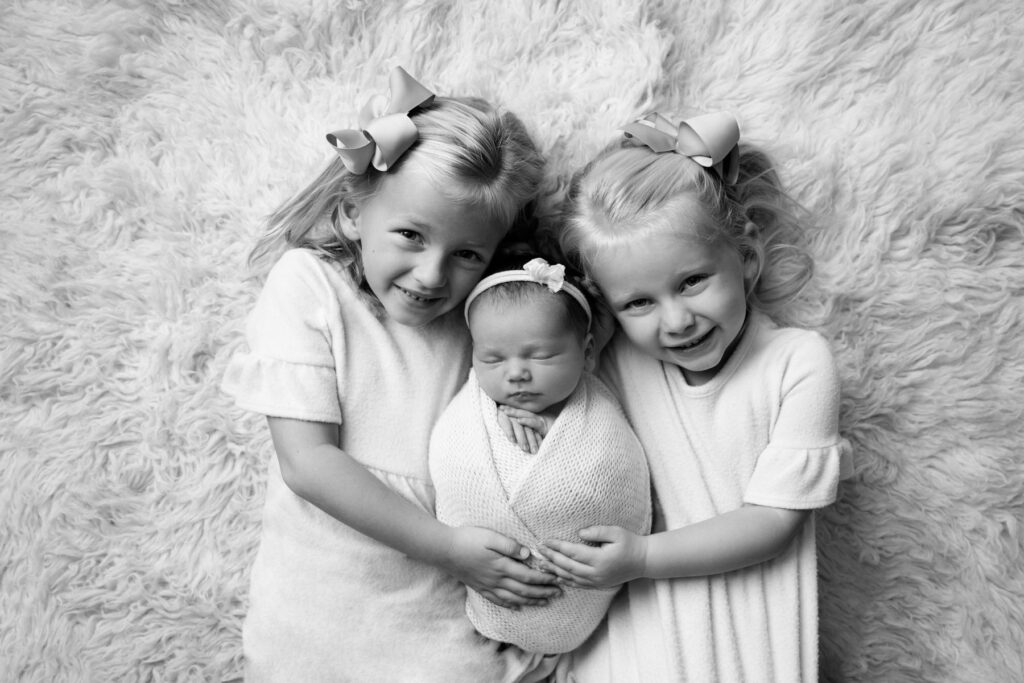 Sisters cuddling their newborn baby sister during a black-and-white newborn photography session