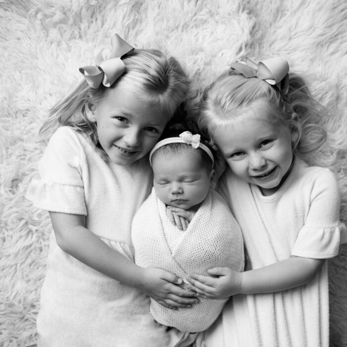 Sisters cuddling their newborn baby sister during a black-and-white newborn photography session