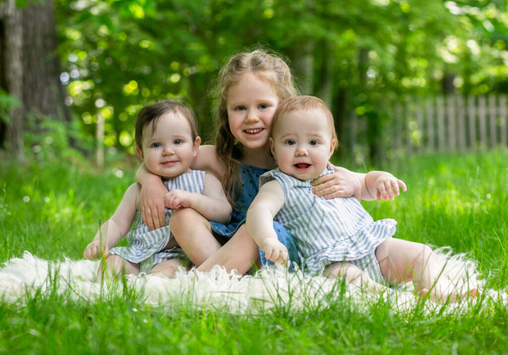 Young girl sitting outdoors with twin baby sisters during a family photography session
