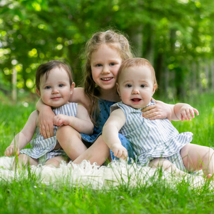 Young girl sitting outdoors with twin baby sisters during a family photography session