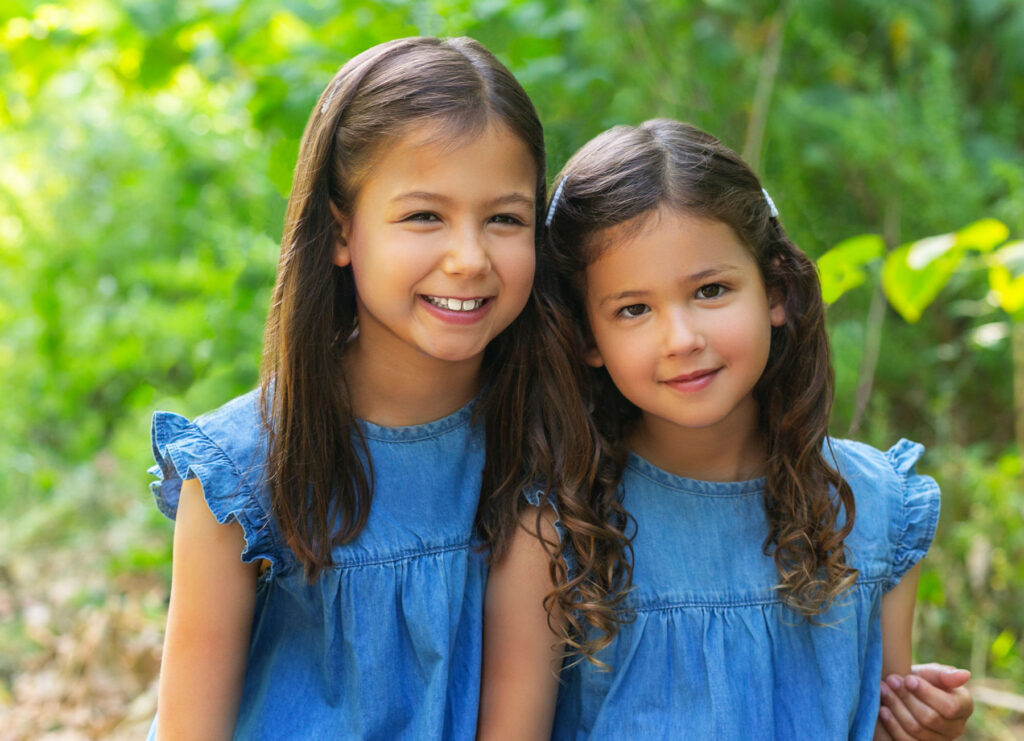 Two smiling sisters photographed outdoors during a Watch Me Grow portrait session.