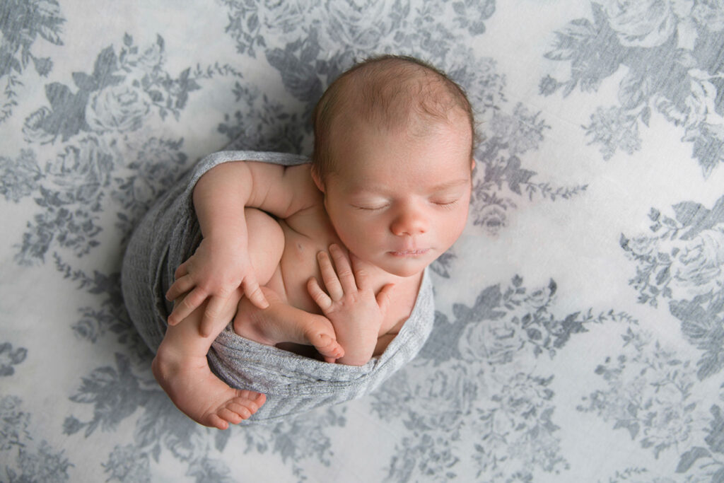 Sleeping newborn baby wrapped in soft grey fabric during studio session